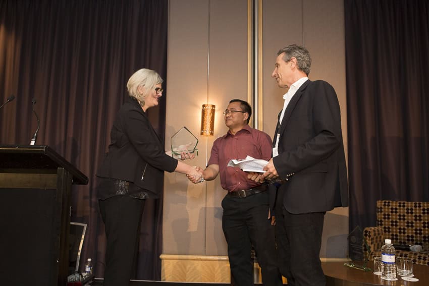 Binota Moy Dhamai shakes hands with Sam Mostyn as he accepts the Sir Ron Wilson Human Rights Award, with Patrick Earle beside them