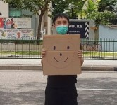 Jolovan Wham wears a mask and holds a cardboard with a drawing of a smiley face outside a Singapore police station in March. Photograph: Jolovan Wham/Reuters
