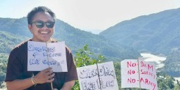 Ebo Mili holding protest sign in the mountains. Credit: FORUM-ASIA