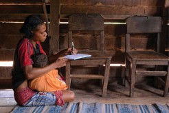 Woman writing a letter at a desk. Still from Papuan Voices. Credit: Fatubun Wensislaus