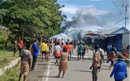 Still of peaceful protest in Nabire, West Papua 5 April 2024. People putting log barrier in road with smoke rising in background. Credit: Rudi Kogoya