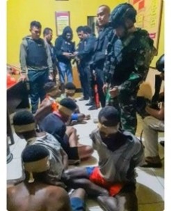 Photo of civilians bound on the floor with military standing over them